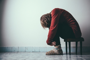 A sad woman stands in front of a brick wall.