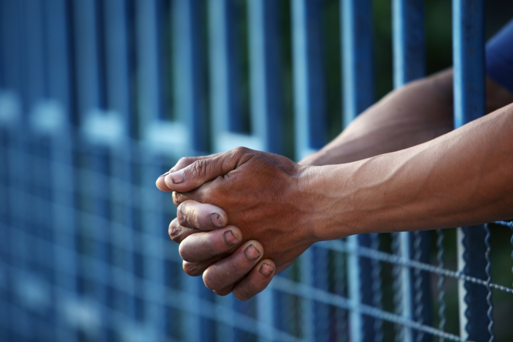 Hands clasped between prison bars