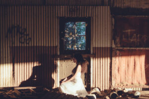 Woman sitting cross legged in room with corrugated walls and scrap metal.