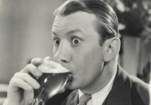 Black and white photo of a man drinking a foamy drink out of a glass.