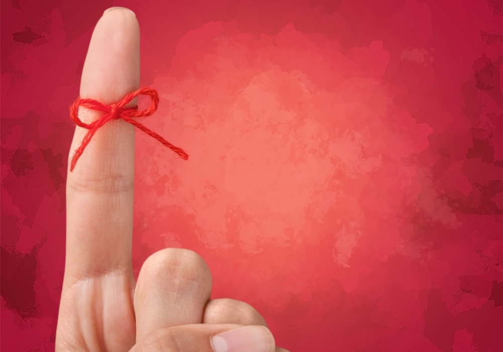 An index finger pointing up with a red string around it.