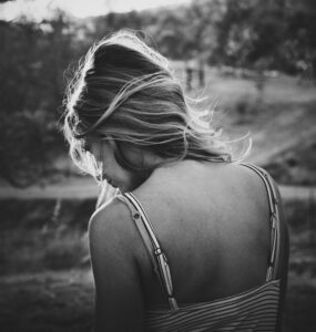 Woman with blondish hair standing with back to camera.