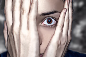 Person with hands covering face, revealing one eye.