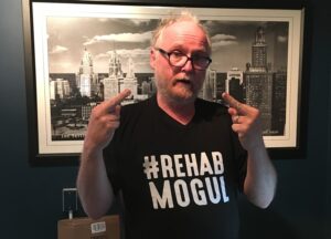 Chris Bathum wearing a tee-shirt saying "Rehab Mogul" and giving the finger to the camera.