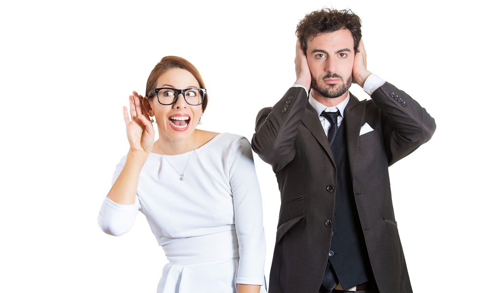 A couple, the woman is listening and the man is covering his ears.