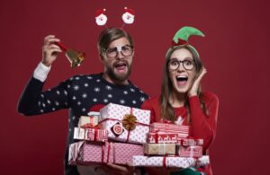 A goofy man and woman in Christmas clothing holding presents and making silly faces.