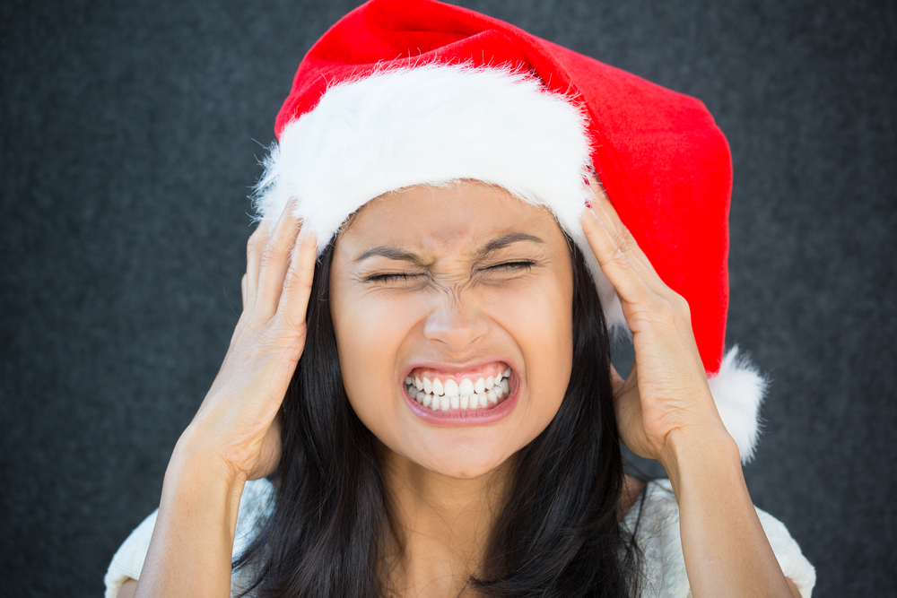 A woman in a Santa hat holding her forehead and grimacing