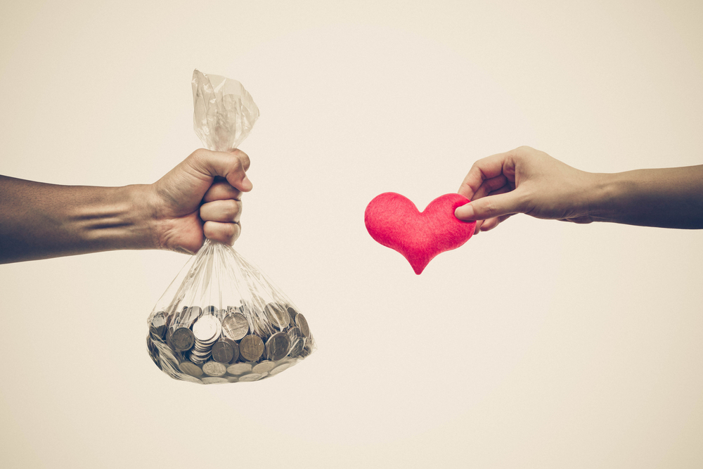 Hands exchanging a bag of coins for a heart.