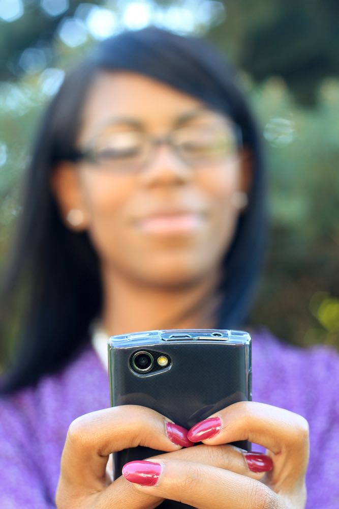 A woman's blurry face with in-focus hands holding mobile phone.