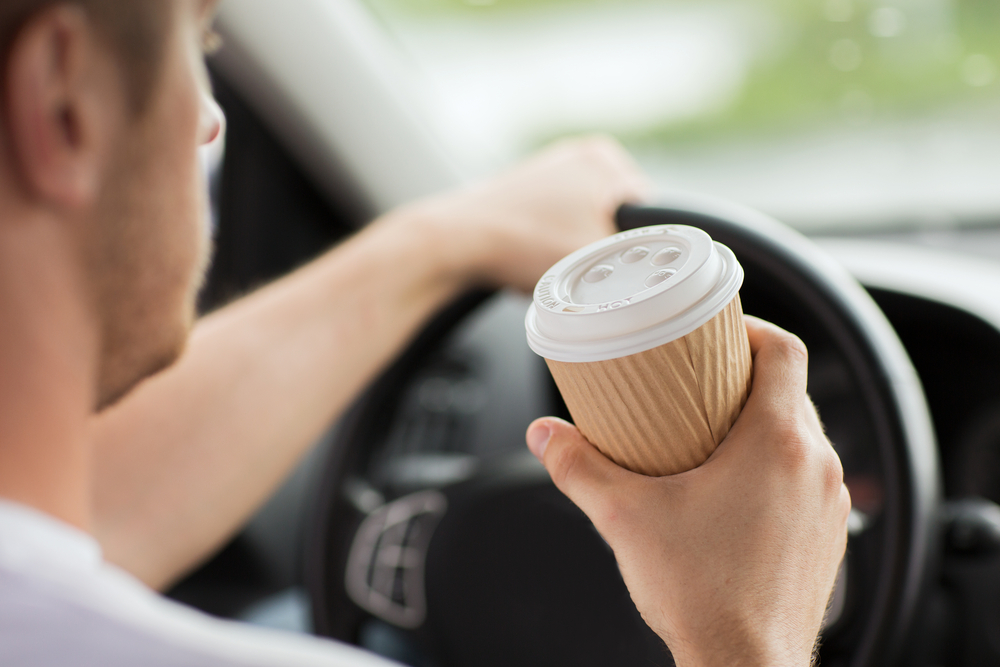 Man holding cup of coffee while driving.