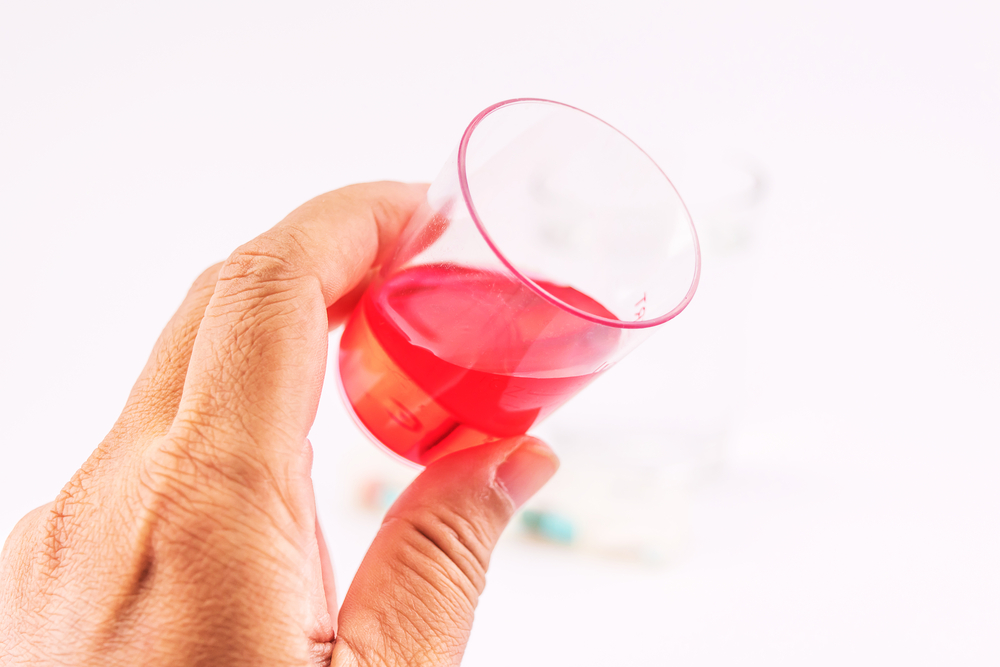 A hand holding red liquid in a clear cup