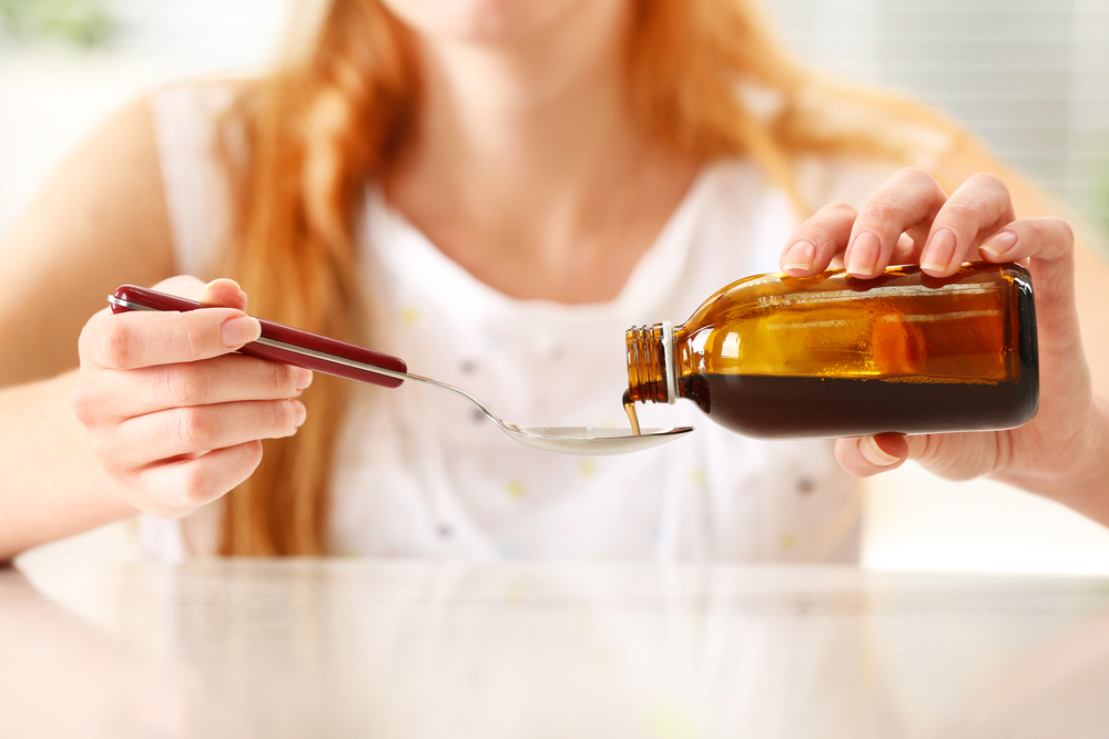 Woman pouring spoonful of medicine.