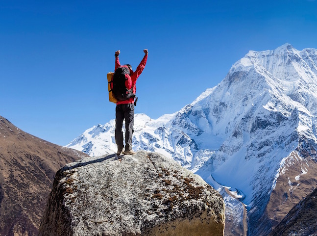 A man atop a snowy mountain, raising hands in victory
