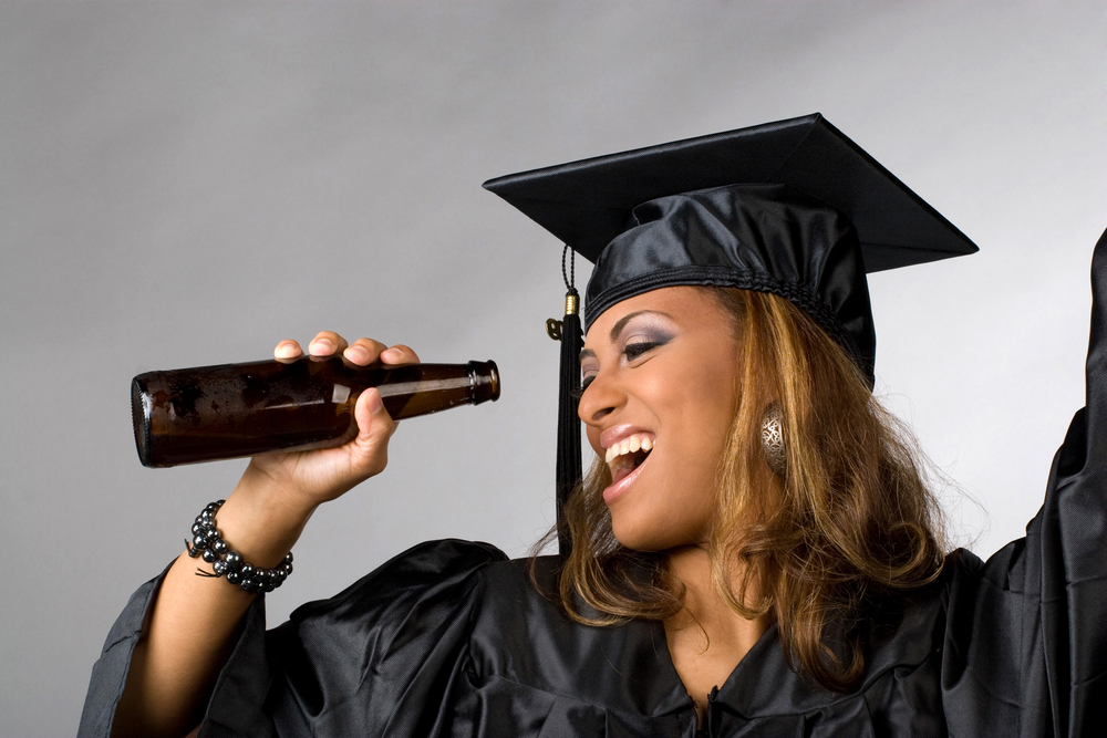 A woman in cap and gown looking into a bottle.