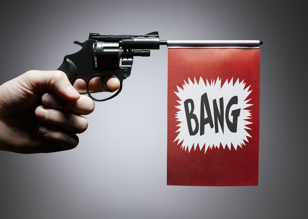 A hand holding a gun with a "BANG" flag coming out of the barrel