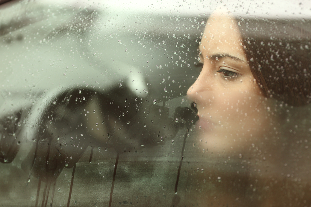 Sad woman looking through car window.