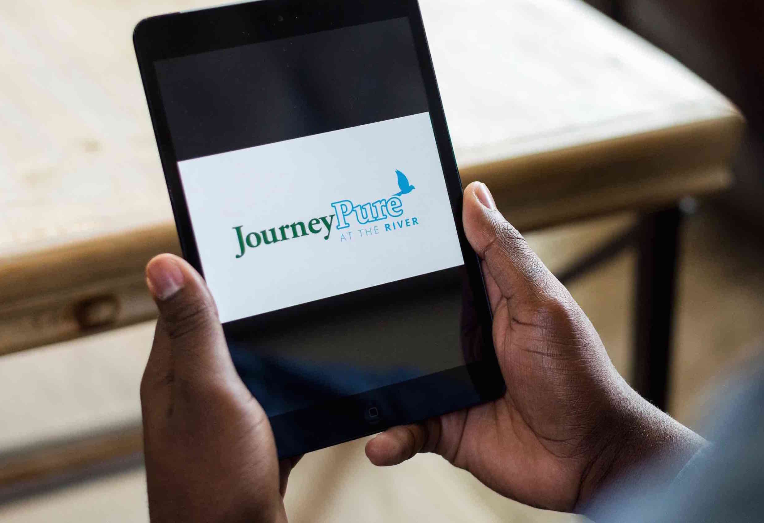Hands holding a phone or device with the JourneyPure logo on the screen