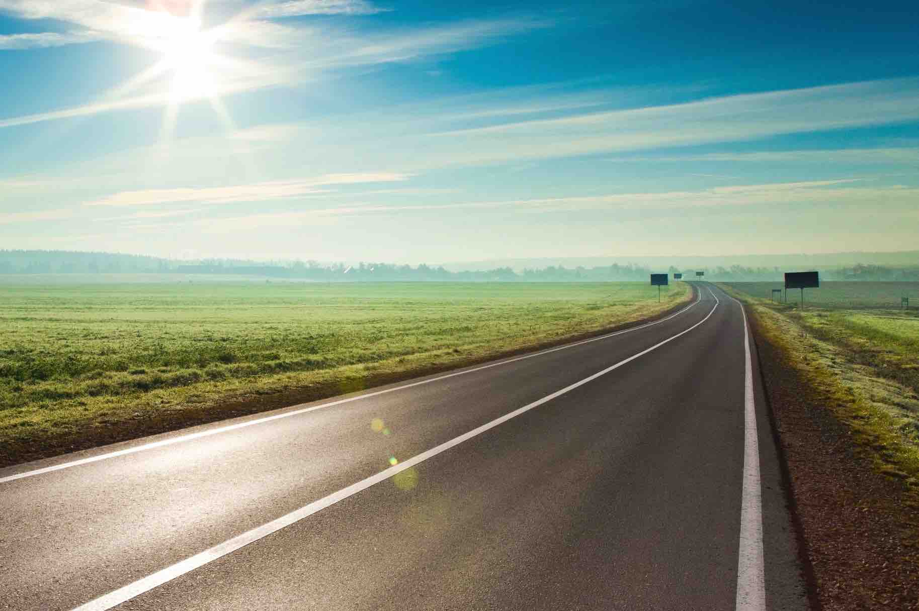 Sun shining down onto a highway in the middle of green fields