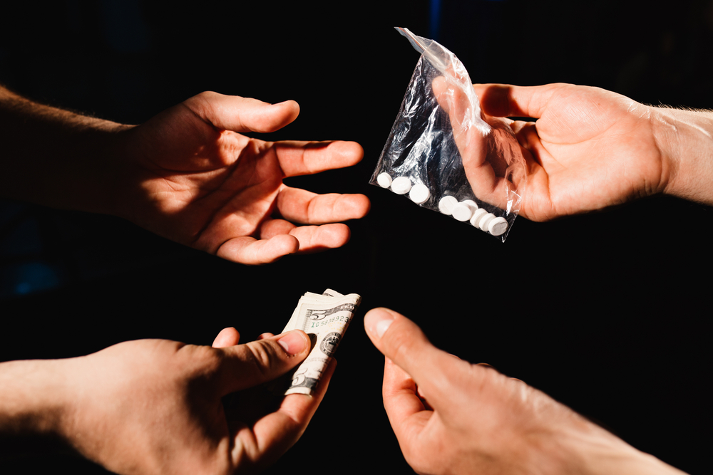 2 people exchanging pills for money in a drug deal.