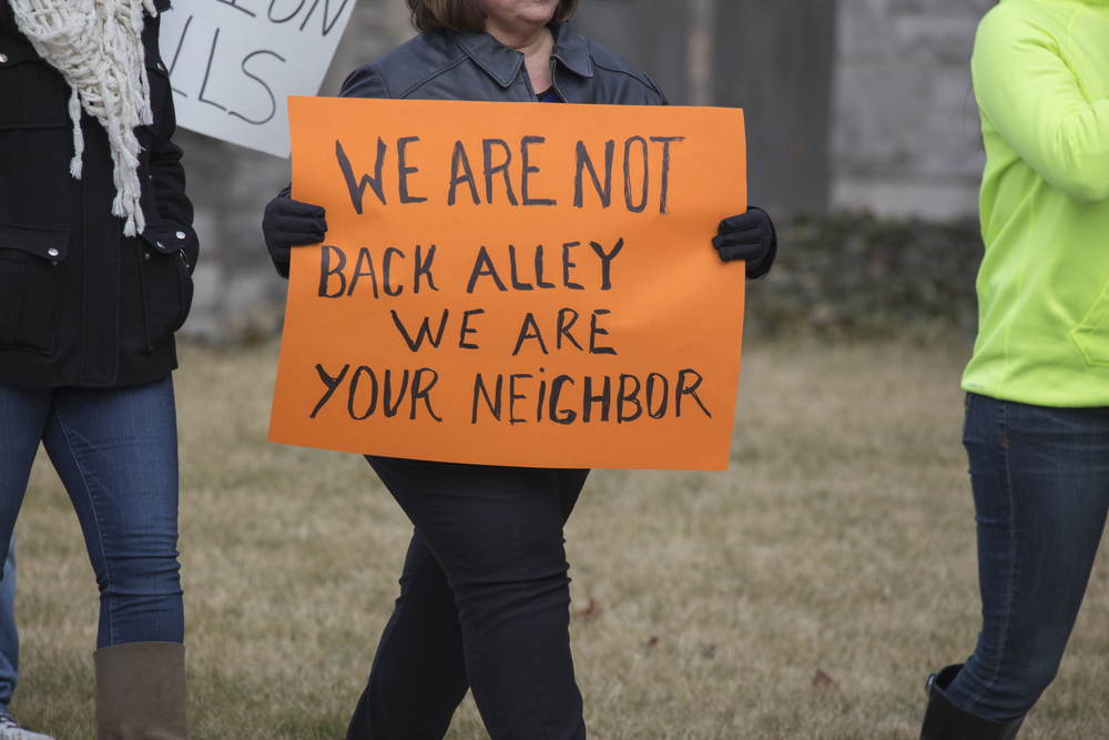 A woman holds a sign protesting bad treatment of addicts.