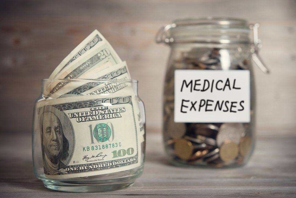 Some hundred dollar bills and a jar with coins labeled "Medical Expenses."