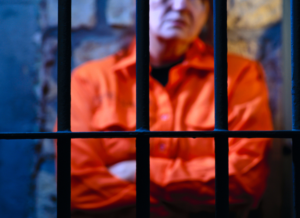 An inmate standing inside a jail cell with his arms crossed.