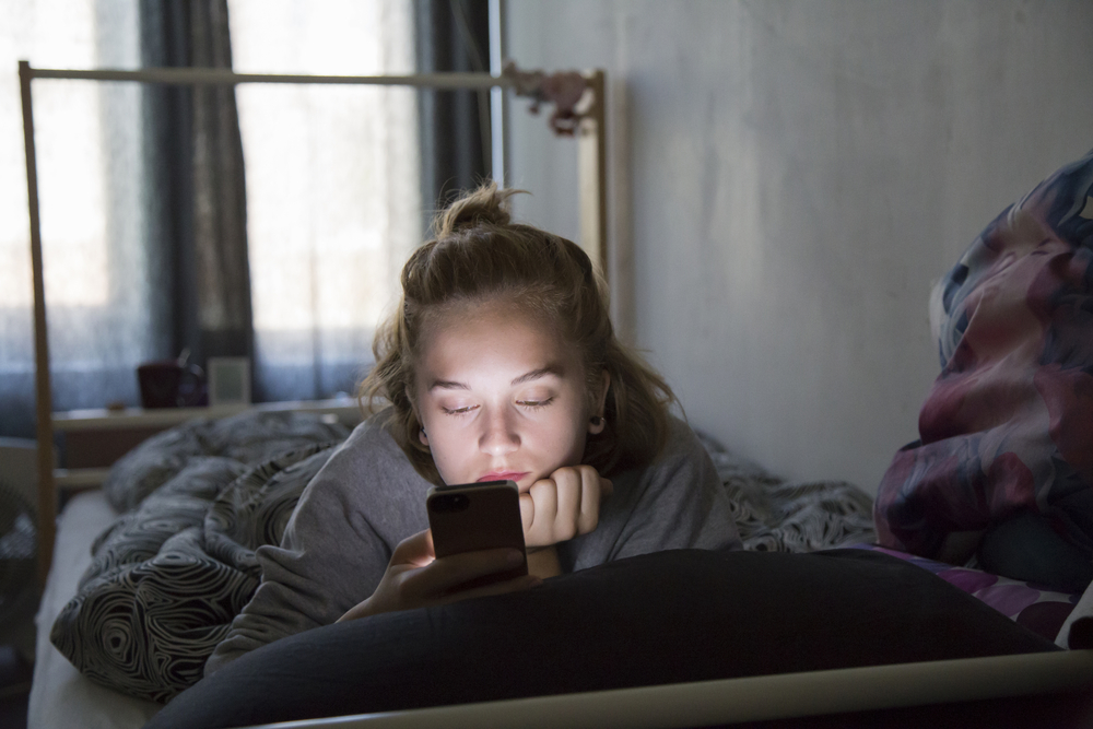 A teenager checking her smartphone in bed.
