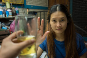 A young woman holding her hand up to refuse an offered beer