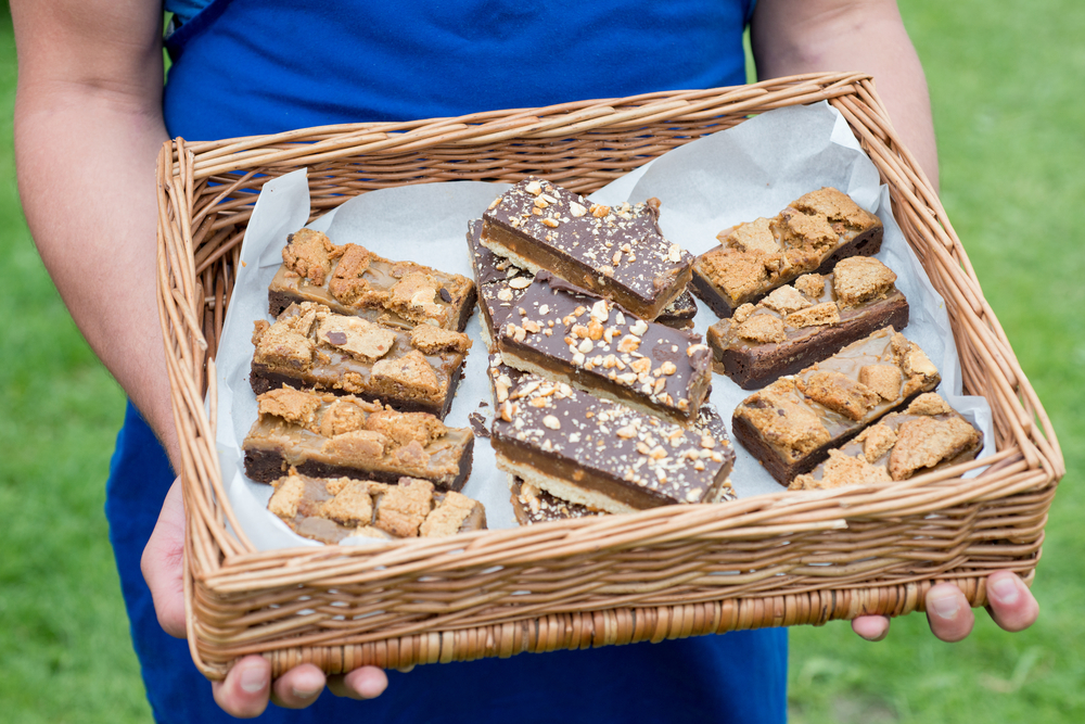 Person holding a wicker basket containing slices of homemade brownies with chocolate nuts and caramel.