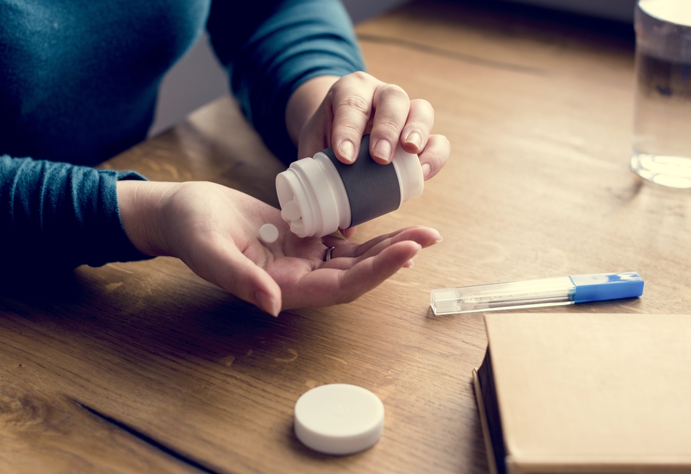 A woman pouring a pill from a medicine bottle into her hand.