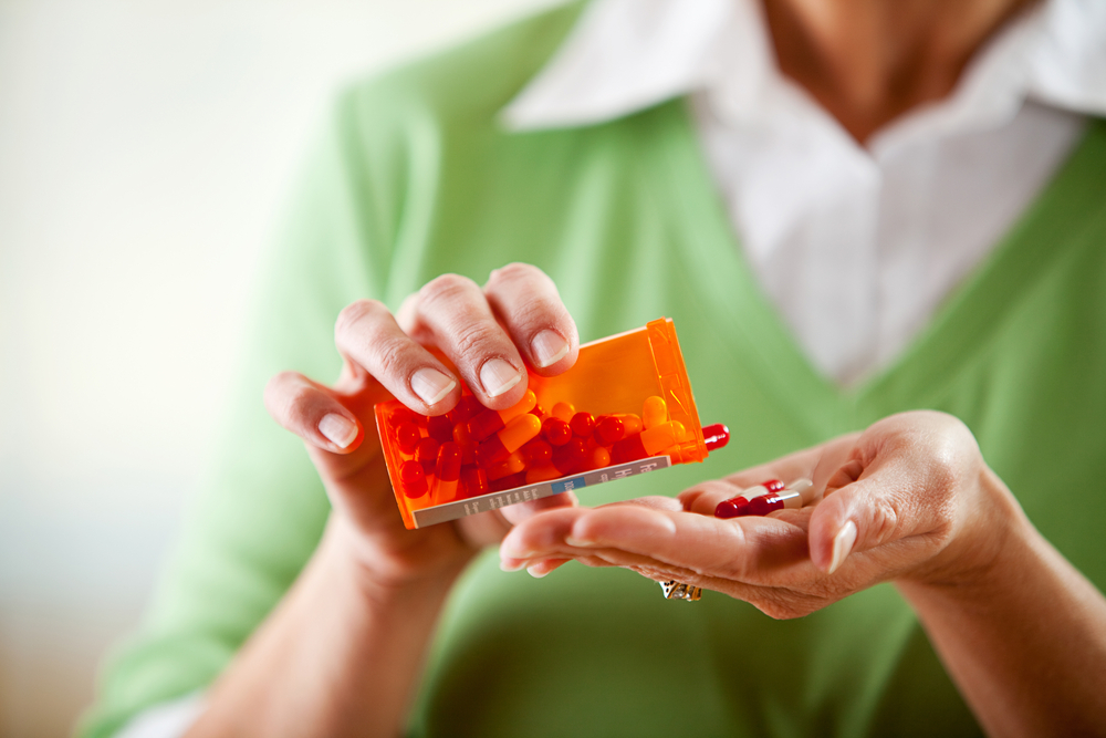 Woman pouring prescription pills from a bottle and into her hand.