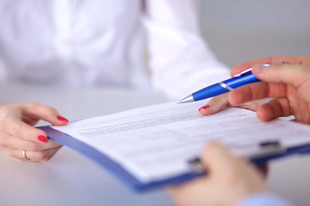 A doctor passing a clipboard with paperwork to a patient.