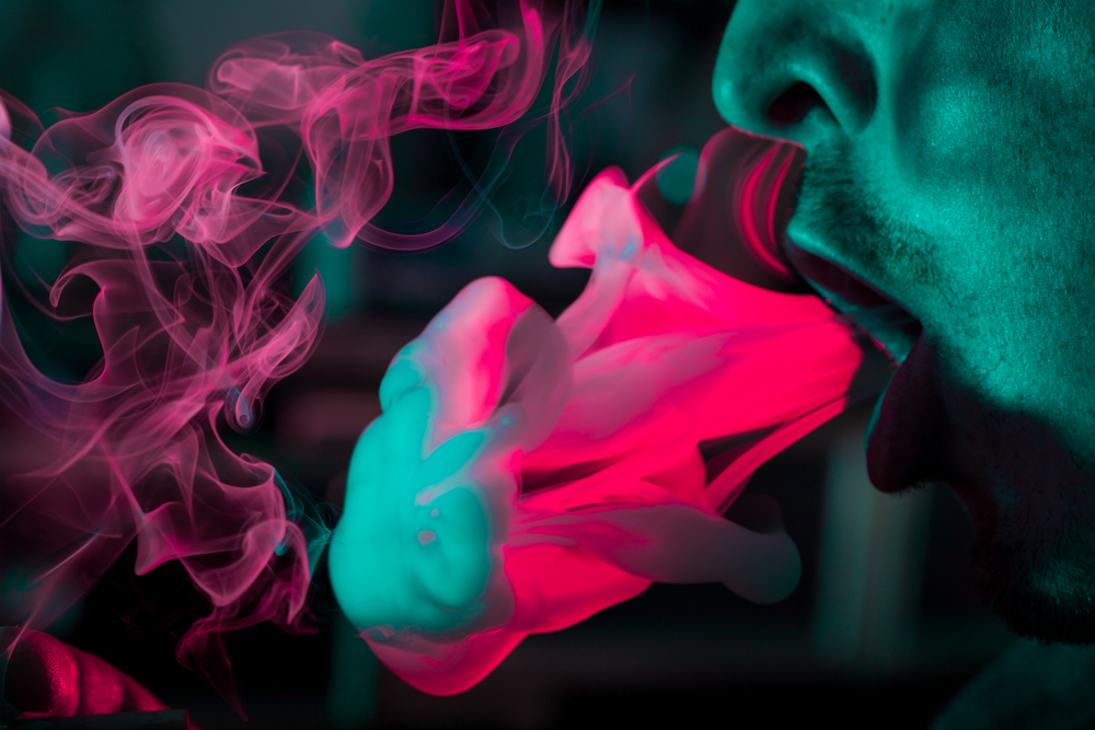Woman exhaling a plume of smoke against a colorful background.