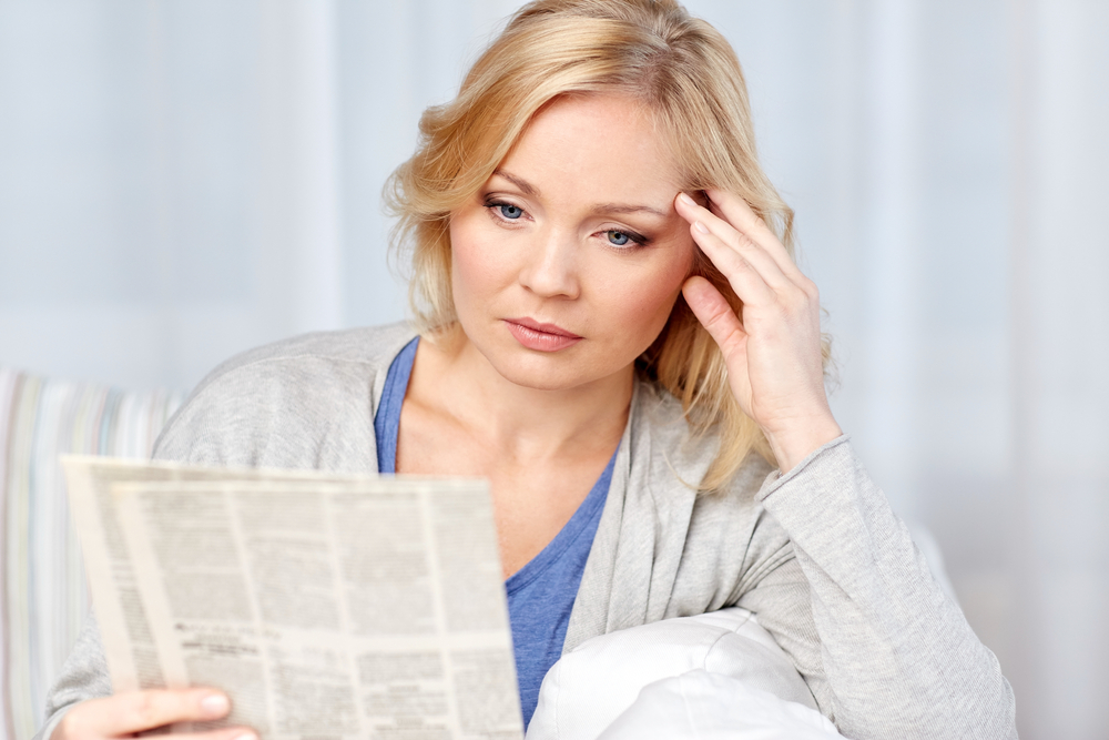 A woman holding a newspaper, looking depressed.