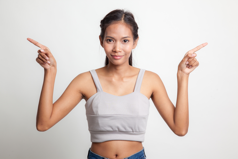 A woman standing and smiling at the camera, fingers pointing outward.