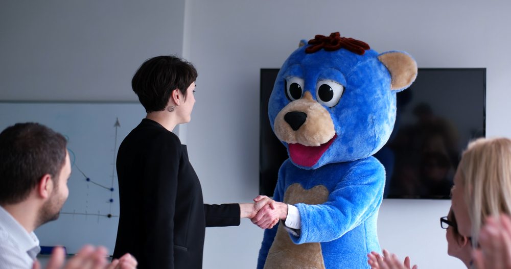 A woman shakes hands with someone in a blue bear character costume.
