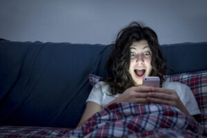 Woman losing sleep while checking her smartphone in bed.