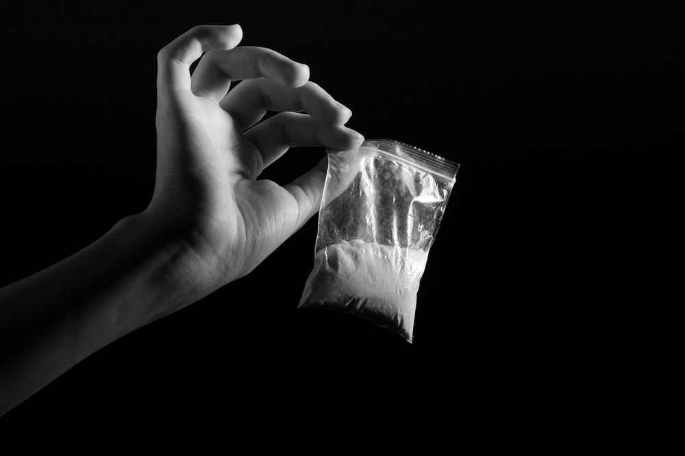 black and white image of a hand holding a bag of narcotics.