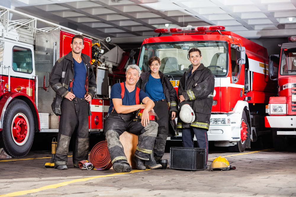 A group of firefighters posing inside of a fire station.