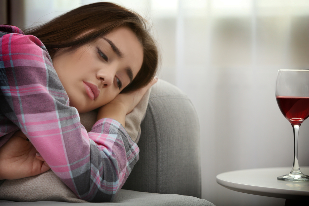 sad woman lying in bed with wine next to her