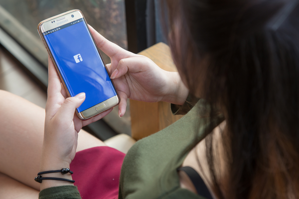 Woman looking at the login screen of a Facebook app on her cell phone.