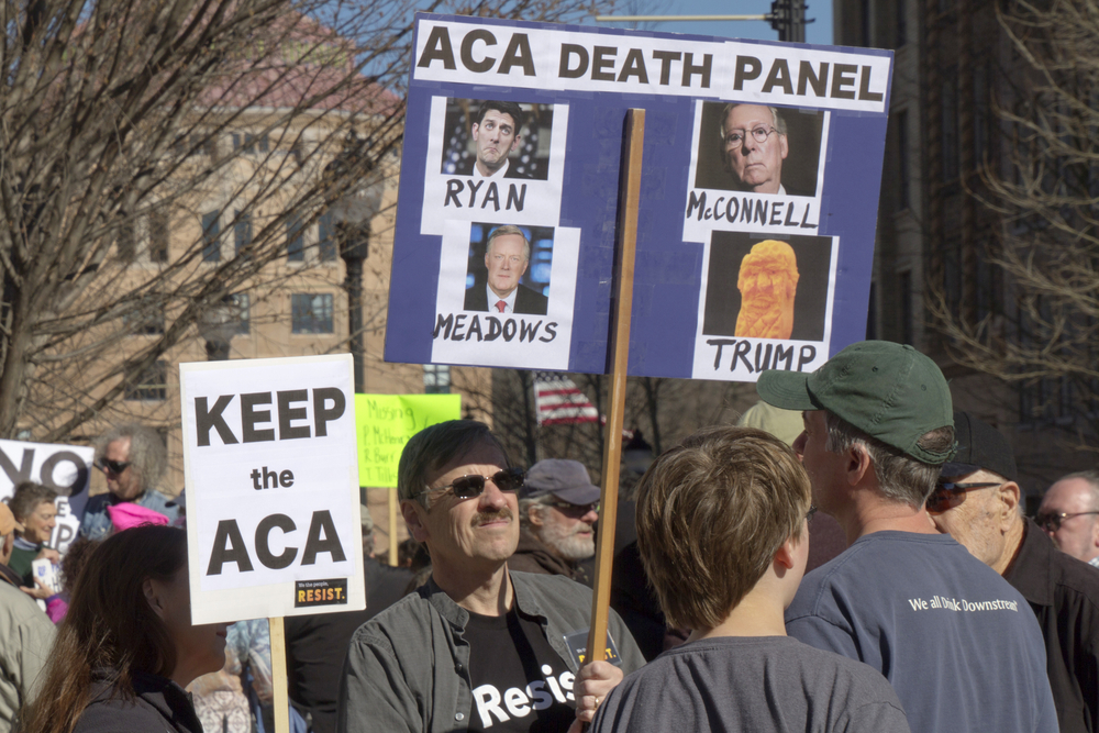 Obamacare activists hold signs saying Republicans Mark Meadows, Paul Ryan, Mitch McConnell and President Trump are the real ACA Death Panel