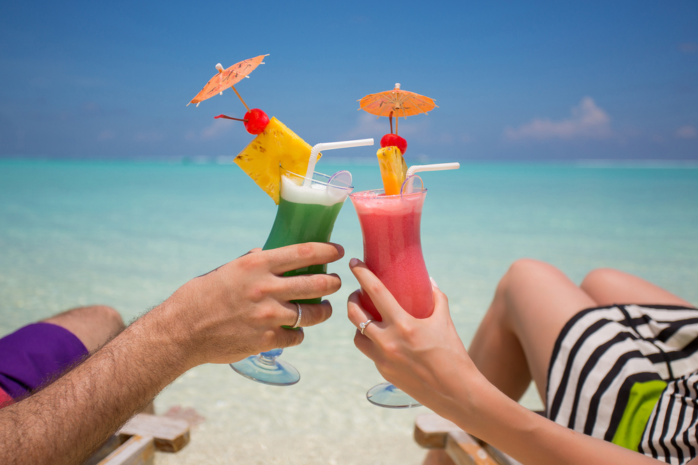 A man and woman toasting with colorful cocktails on a beach