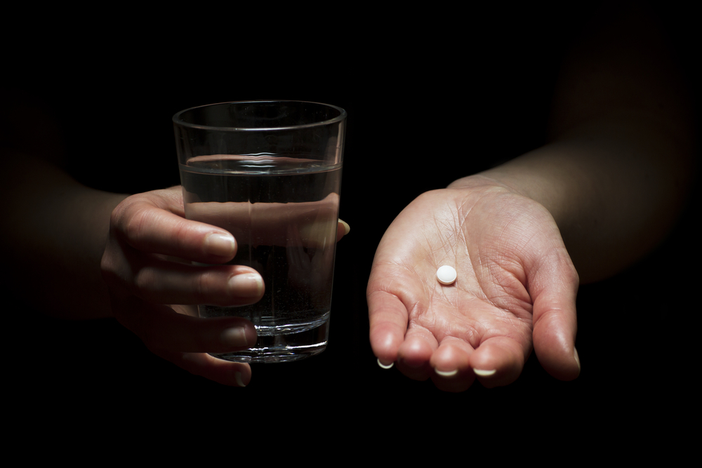Woman holding a glass of water and pill.