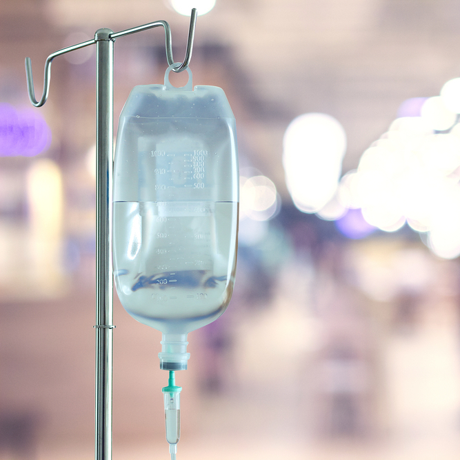 Hanging saline bag in focus on blurry hospital in the background