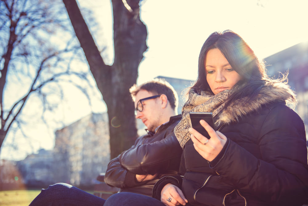Serious woman sitting in park next to man