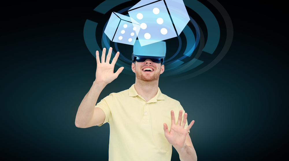 happy young man with virtual reality headset or 3d glasses playing game with casino dice projection over black background