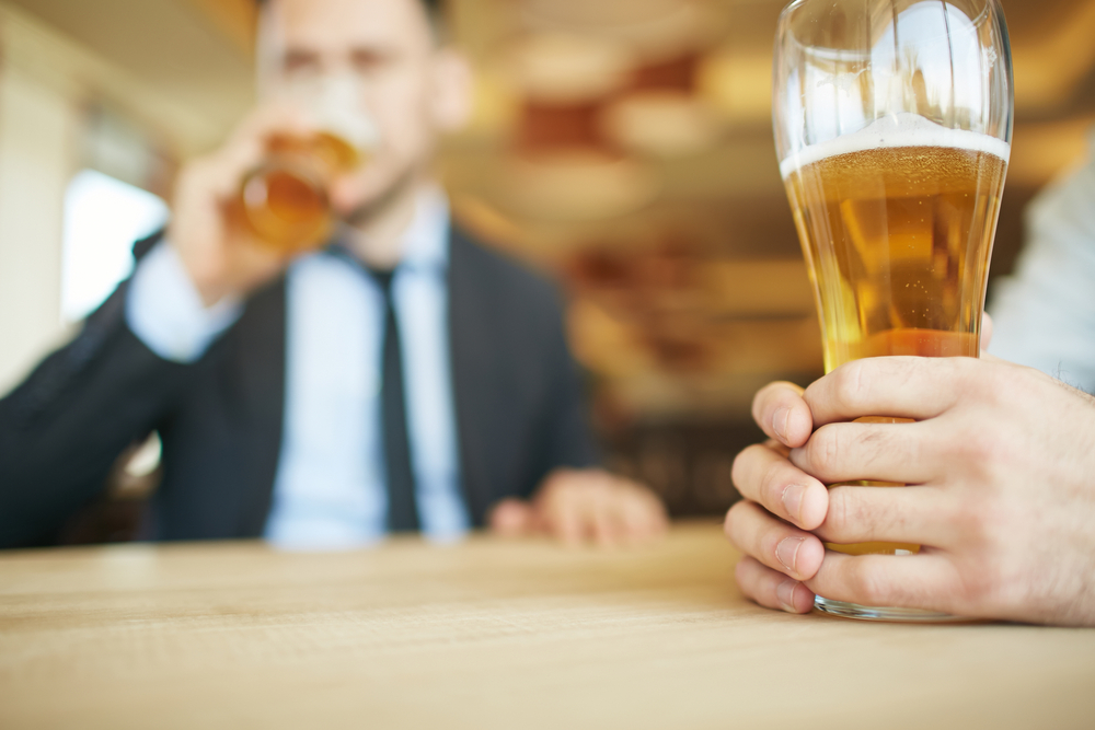 Close-up of beer glass and businessman drinking in the background