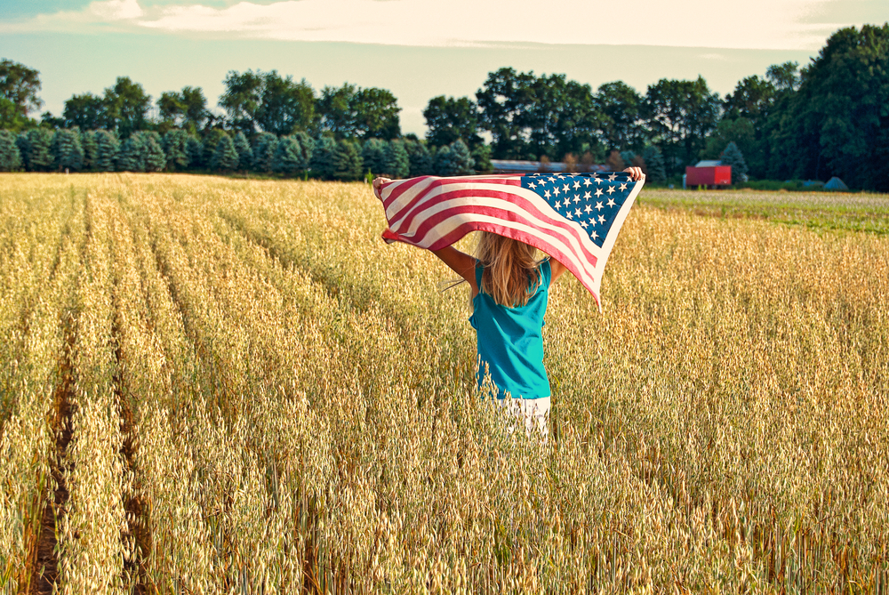 girl running through wheat field with American flag