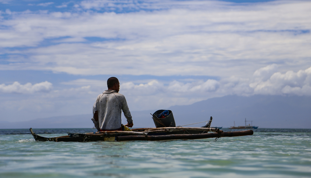 A fisherman rows his wooden raft off the coast of the Philippines.